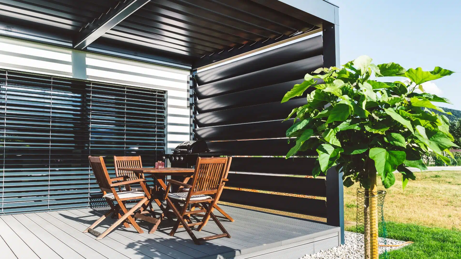 Modern Louvered Pergola with Outdoor Dining - enVision Pergola Contemporary black pergola with wooden table and chairs on a patio, featuring a large potted plant.
