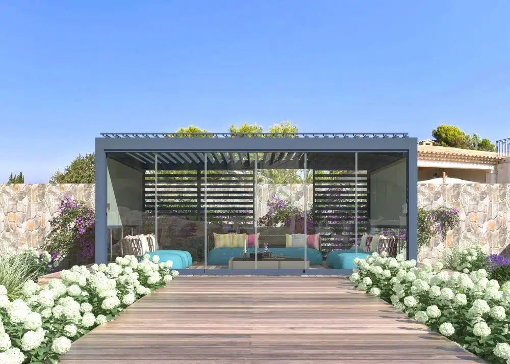 Modern louvered pergola with glass walls and a cozy seating area surrounded by flowers and stone walls in a landscaped garden