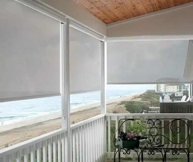 Covered porch with white solar shades providing shade and privacy while overlooking a scenic beach view