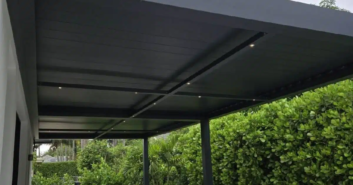 Recessed Pot Lighting for Luxury Pergolas - enVision Pergola A view of a black louvered pergola ceiling at dusk featuring small, warm recessed LED pot lights installed within the structural crossbeams.