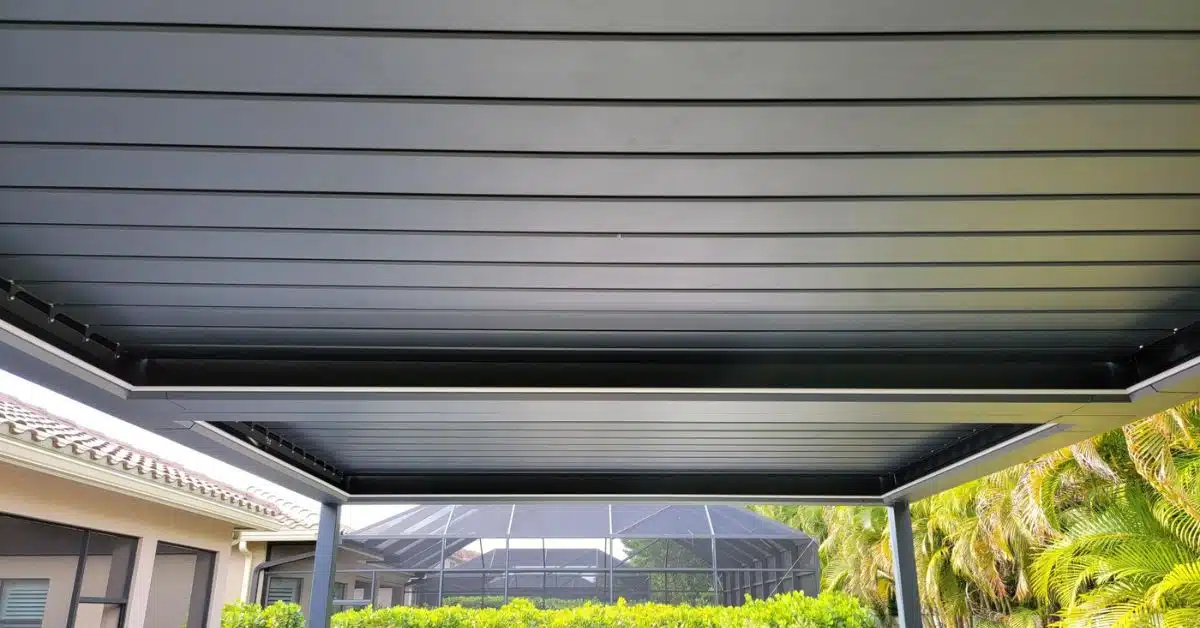 Sleek Black Solid Roof Pergola for Modern Patios - enVision Pergola A close-up view of an all-black solid roof pergola ceiling with deep channels for water drainage, situated next to a residential home and pool cage.