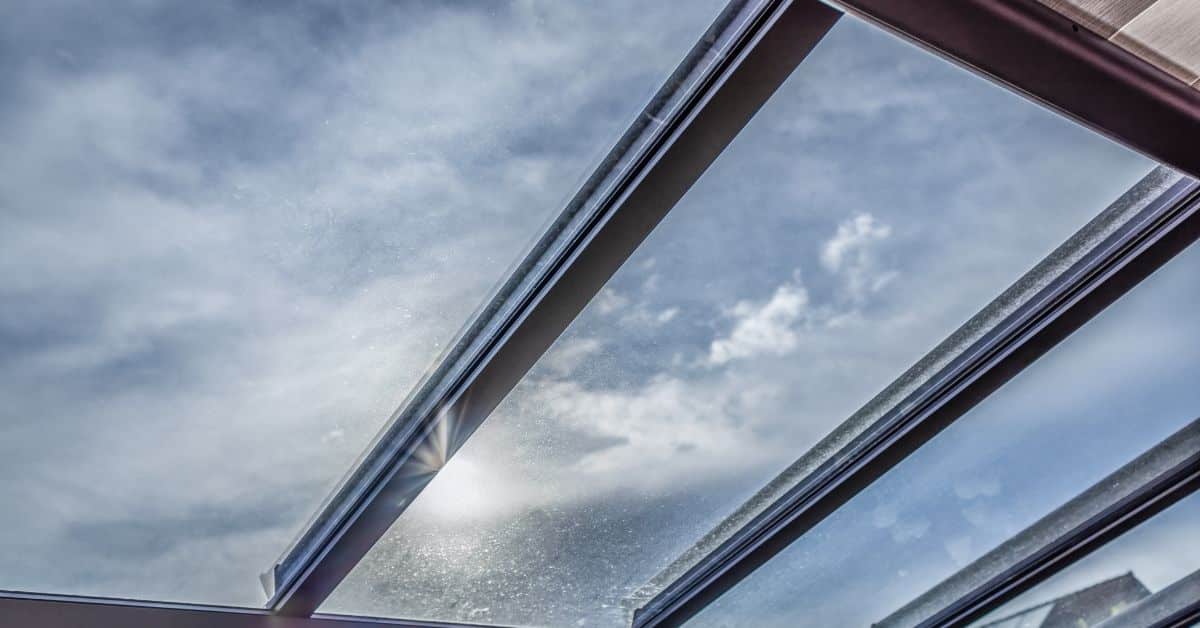 High-Transparency Glass Pergola Roof - enVision Pergola A view looking up through a clear glass solid roof pergola panel, showing a bright sun and blue sky through the high-transparency protective layer.