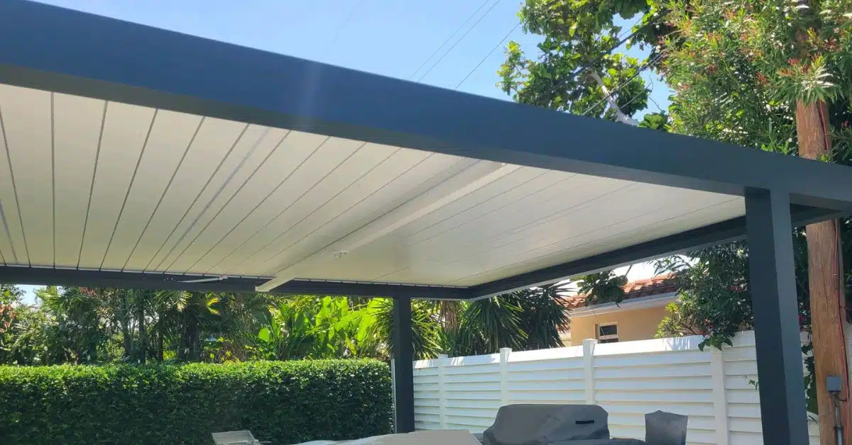 An upward interior view of a modern pergola with a dark charcoal frame and contrasting white solid roof panels, providing full shade over a patio.