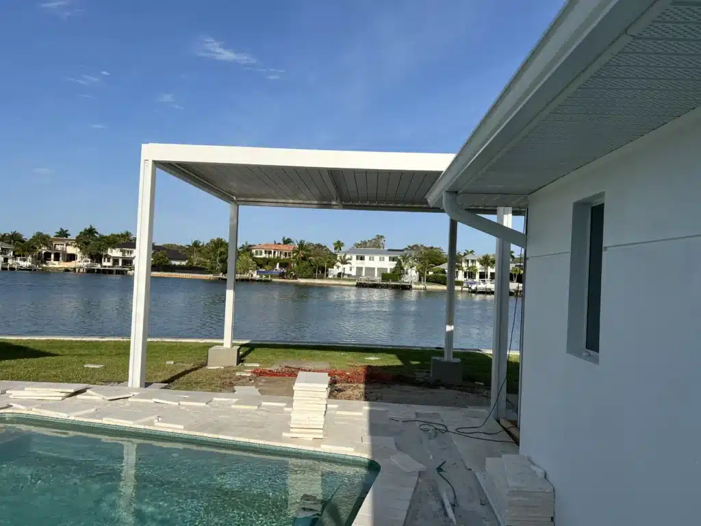Under-construction white patio frame over a pool with a canal-side neighborhood in the background on a sunny day