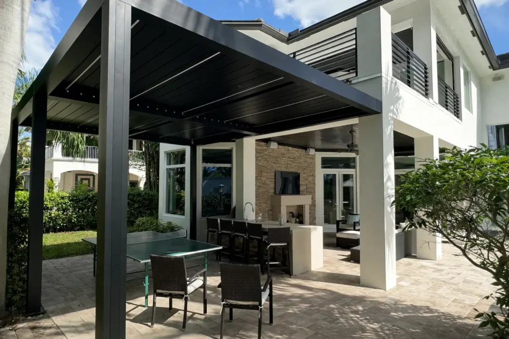 Modern covered outdoor living space with a black metal pergola, dining table and bar seating under a patio of a two-story white house.