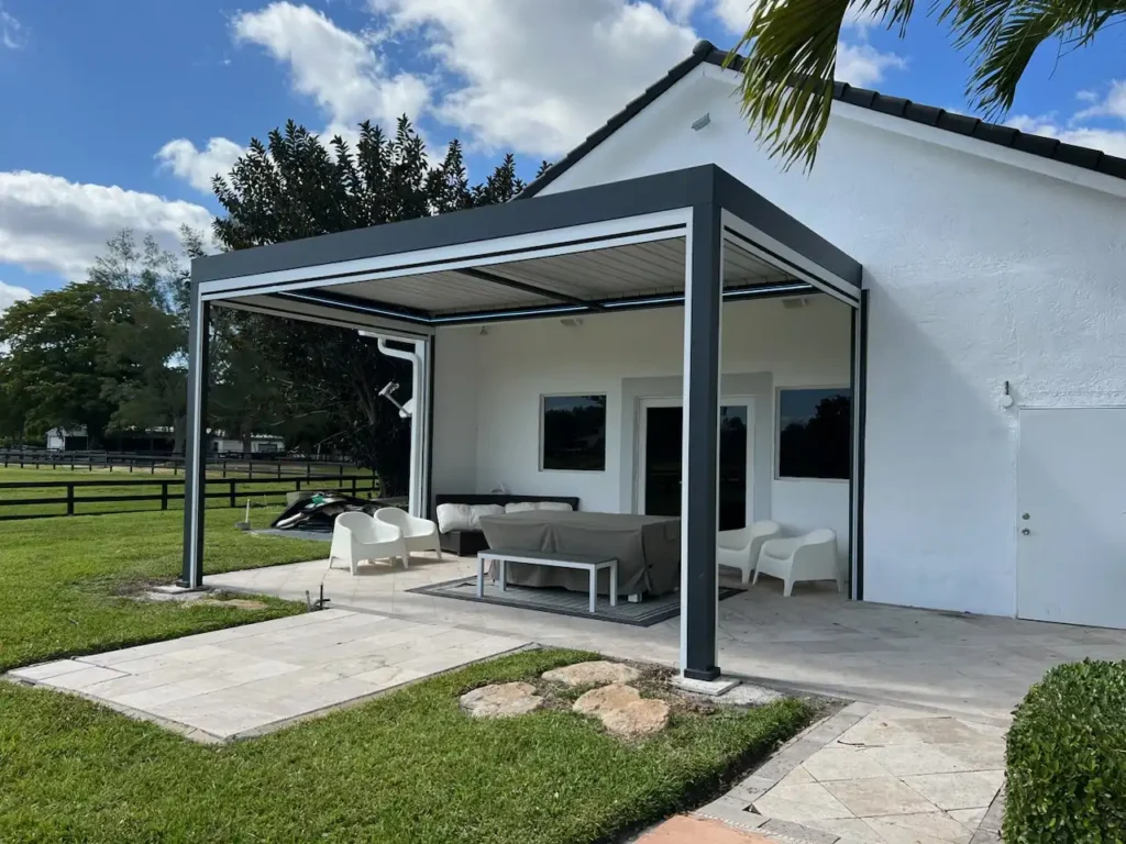 Outdoor patio under a modern gray-framed pergola attached to a white house, with white seating and a coffee table.