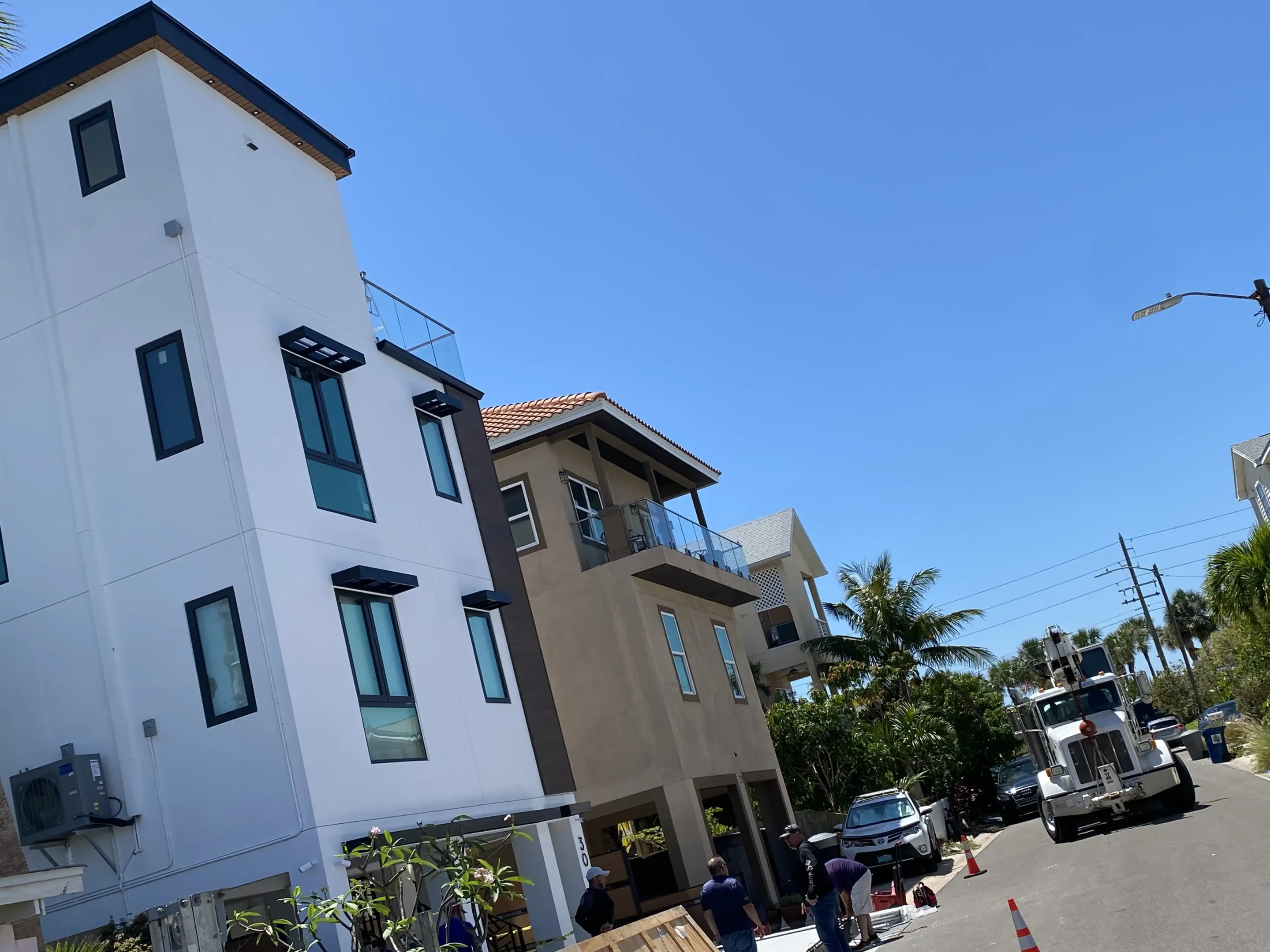 Modern white apartment building with dark trim under construction; workers and a white truck on a sunny day.