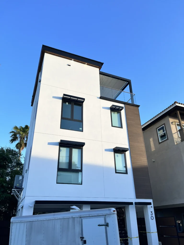 Modern white, multi-story residence with black-framed windows against a clear blue sky.