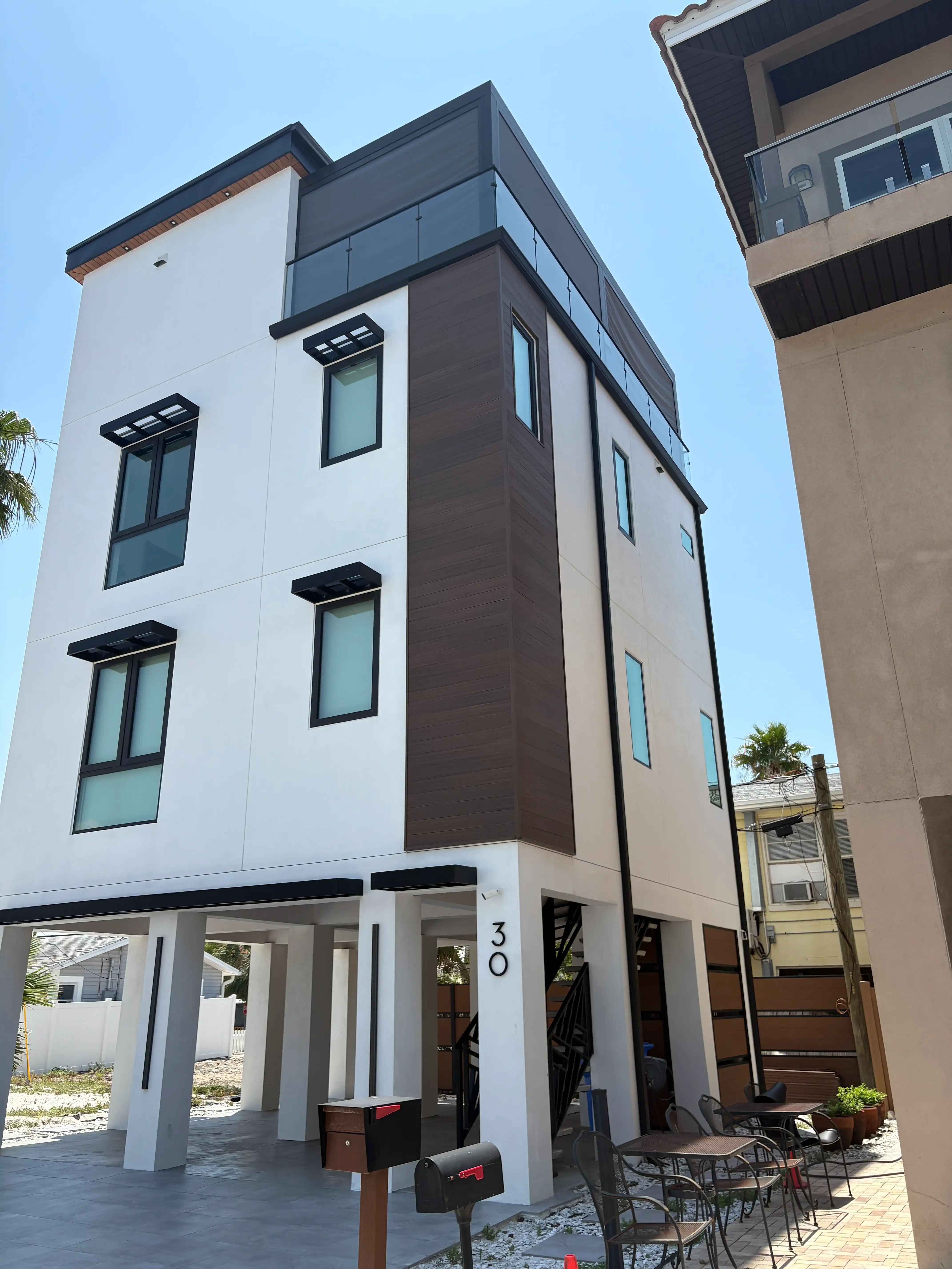 Modern multi-story building exterior with white walls, dark wood panel accents, and glass balcony railings.