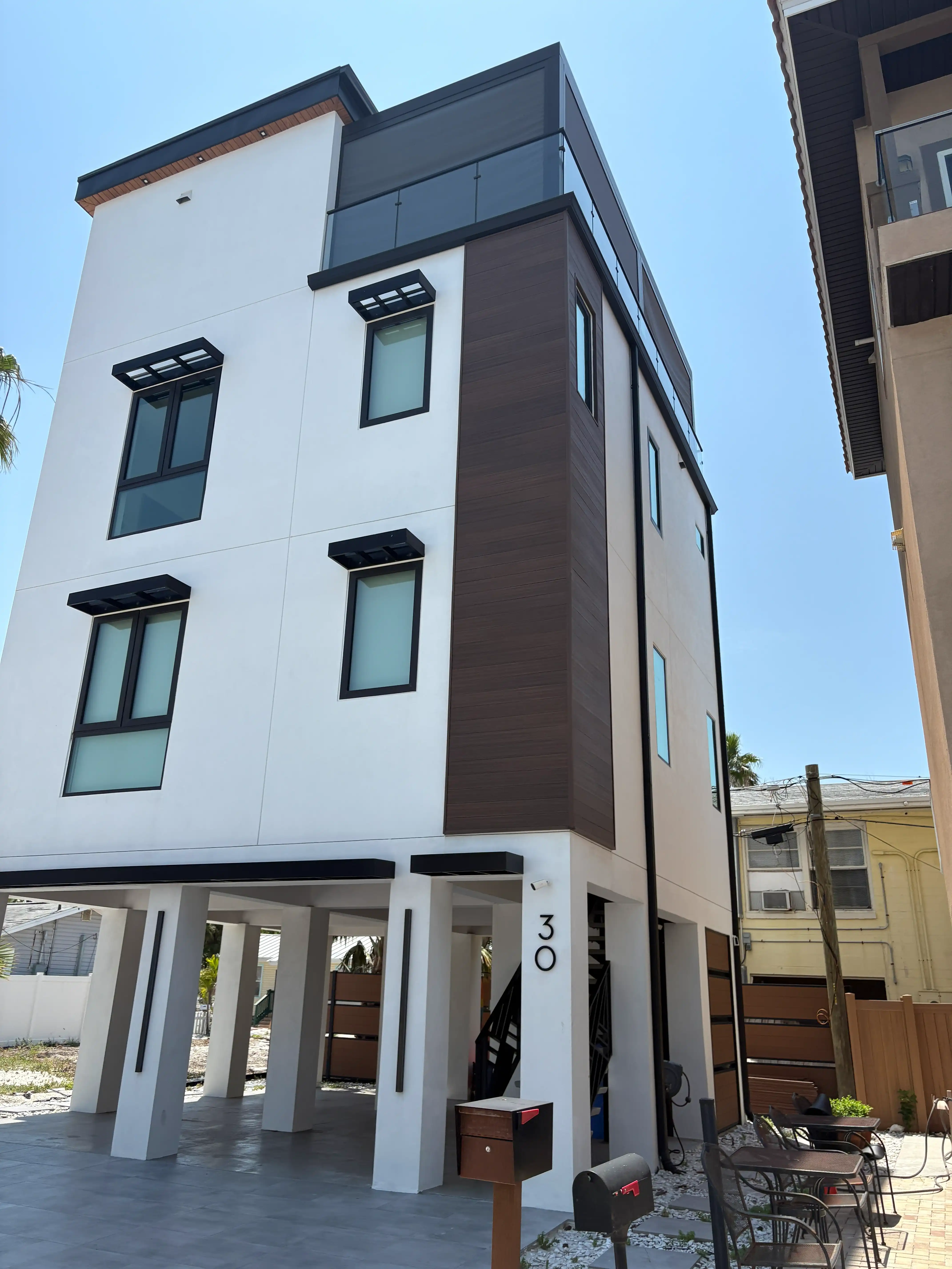 Modern white apartment building with dark brown vertical panels, large windows, and a glass balcony at the top. Typical urban exterior view.