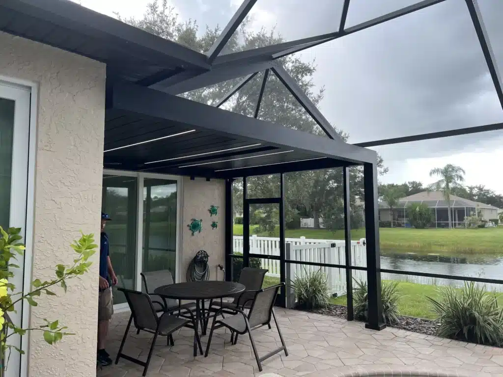 Backyard patio with a black metal dining set under a glass-enclosed screened porch overlooking a lake.
