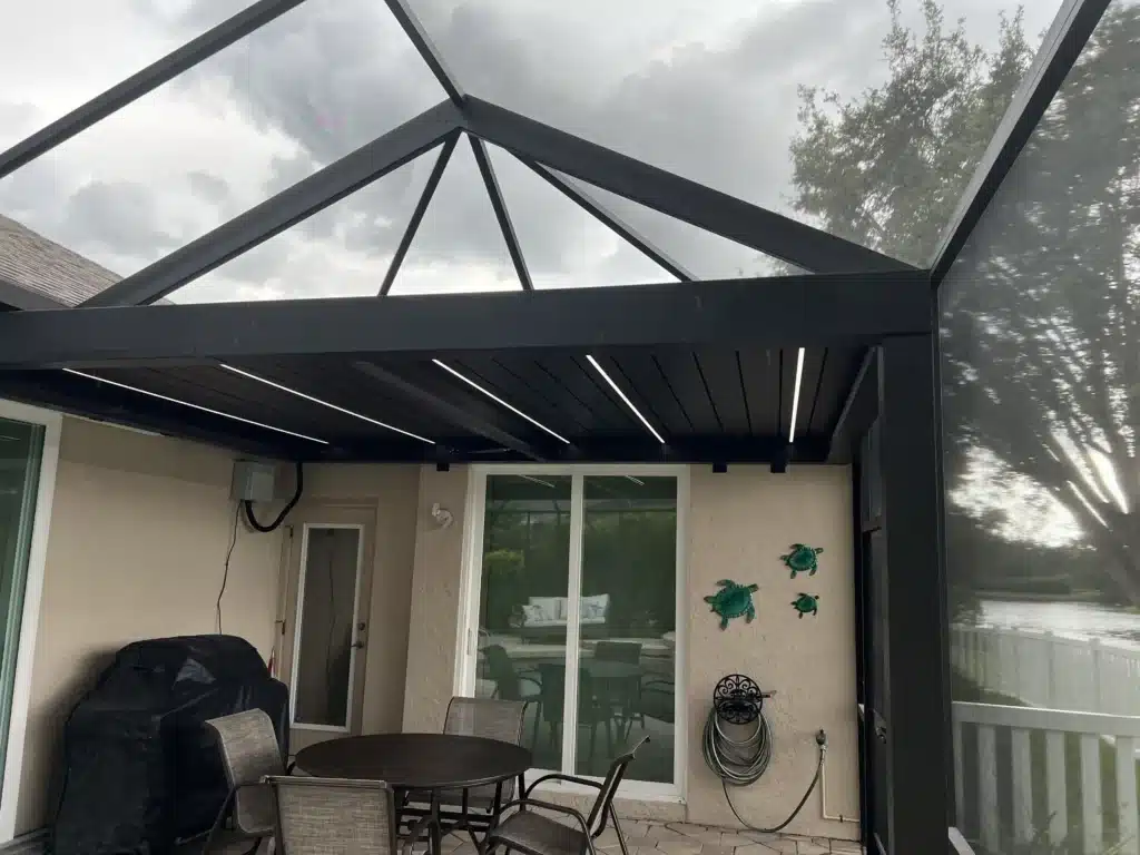 Patio with a metal-framed glass roof and an outdoor dining table set under a cloudy sky.