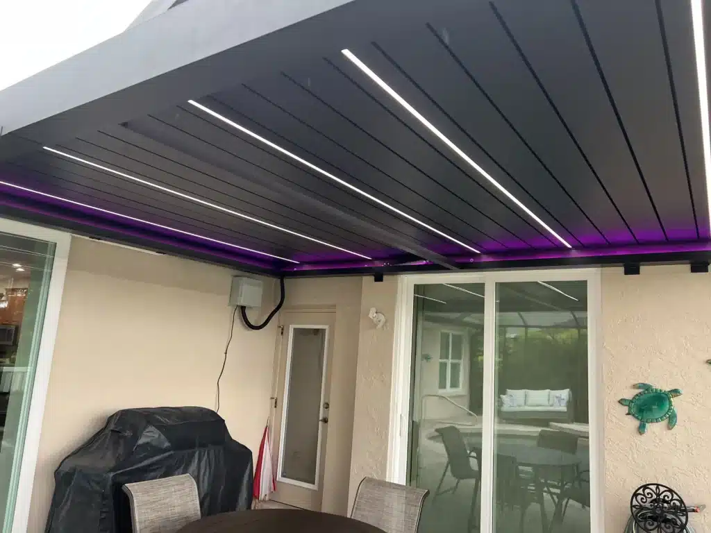 Covered outdoor patio with a slatted dark ceiling and purple LED lighting along the edge, glass doors, and outdoor seating.