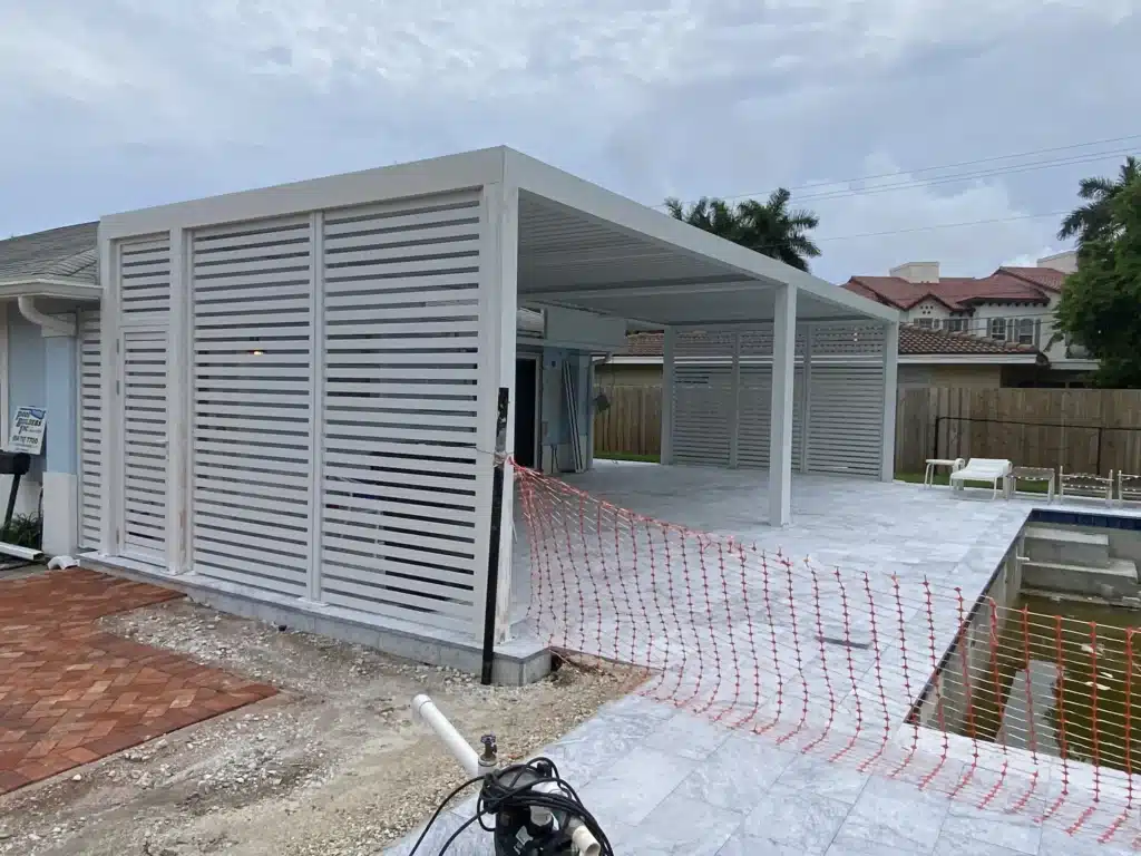 White slatted privacy walls and a white metal canopy over a paved outdoor area under construction in a residential yard.
