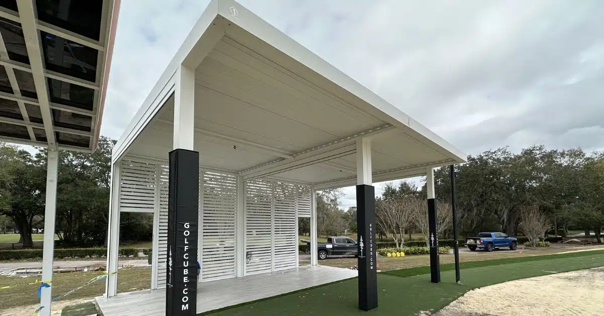 Customized Motorized Pergola for Sports and Leisure - enVision Pergola A white motorized pergola structure with adjustable louvers and slatted privacy walls, used as a professional golf hitting bay on a green turf area.
