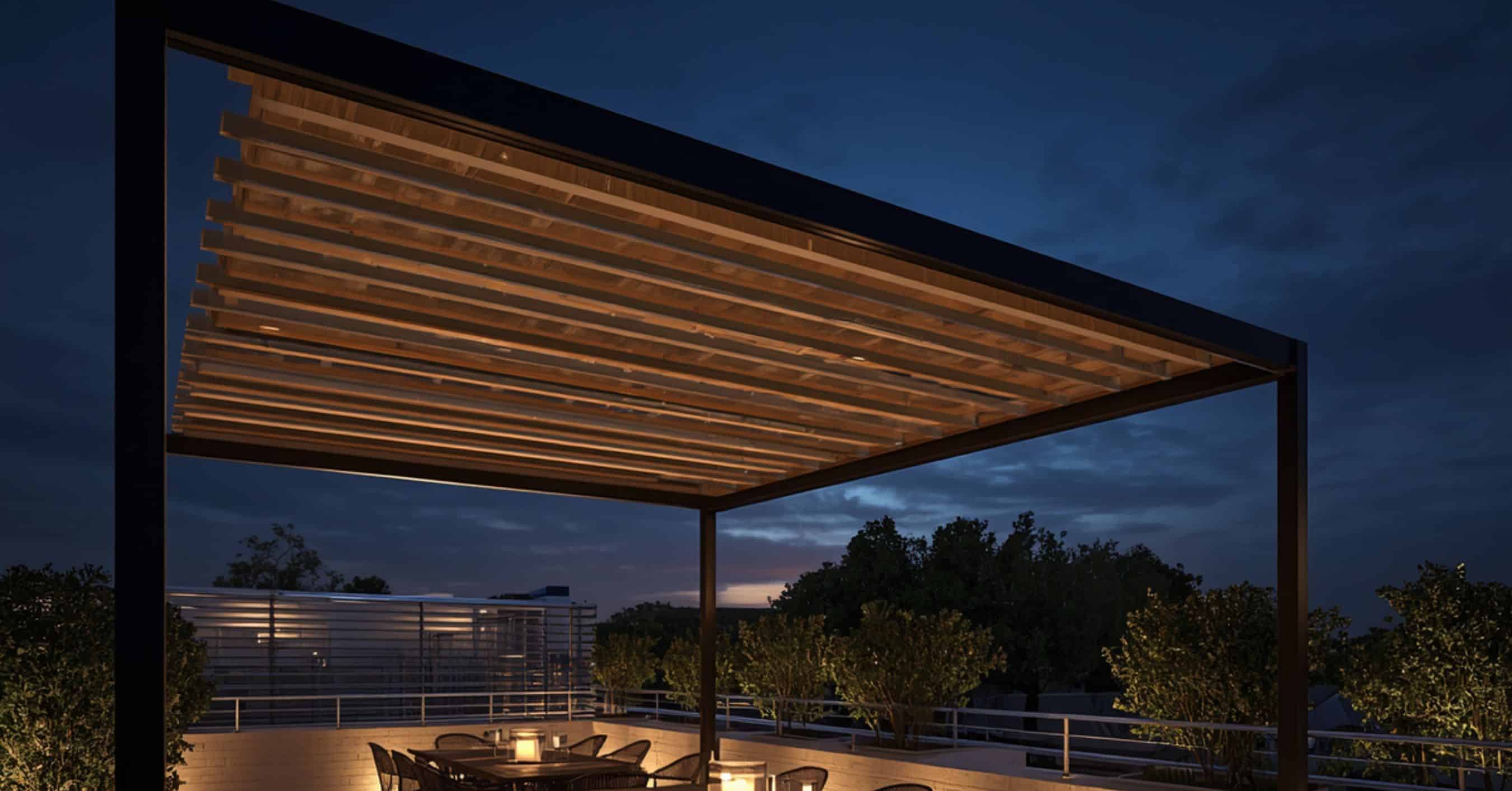 Motorized Pergola with LED Night Lighting Upgrade - enVision Pergola A motorized louvered pergola at night featuring integrated warm LED strip lighting, illuminating an outdoor dining area on a rooftop terrace.
