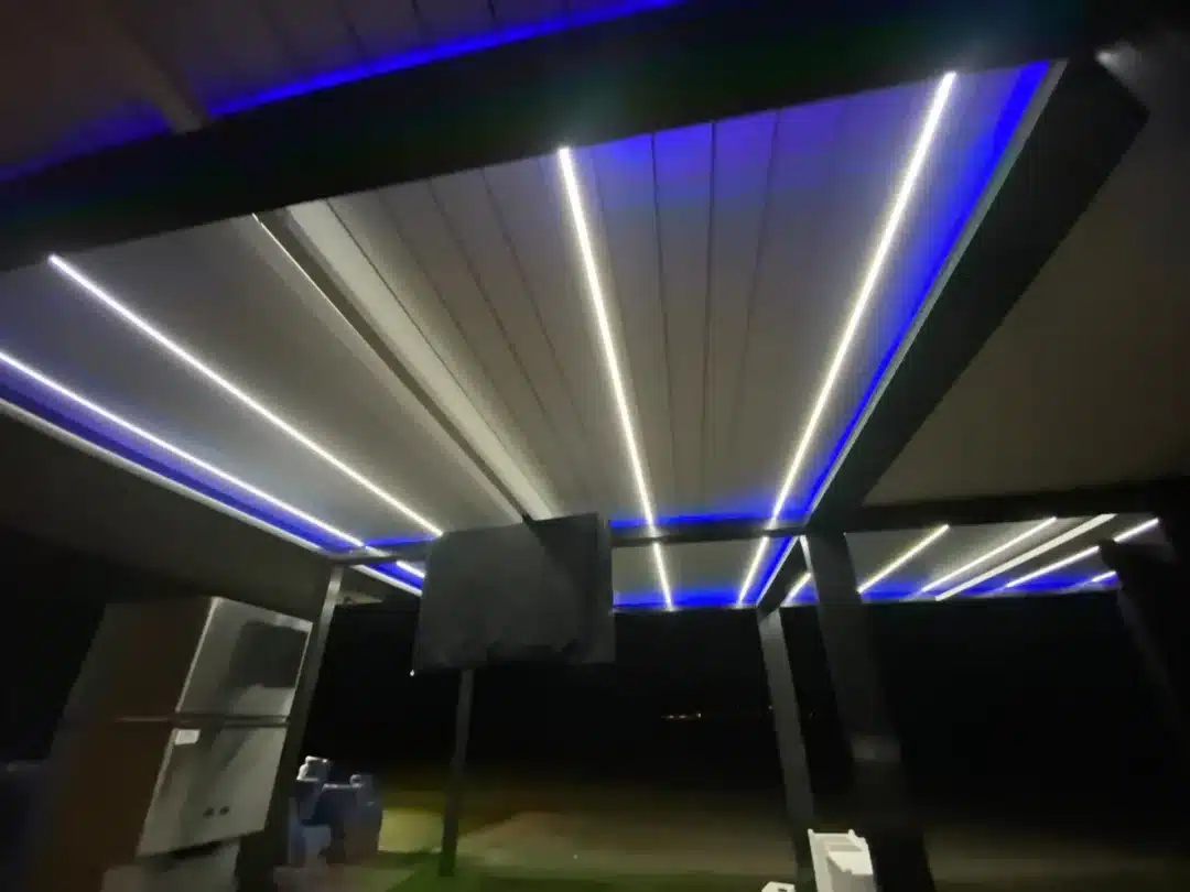 Night view of a modern outdoor area with blue and white LED strip lighting along a roof—the ceiling panels glow.