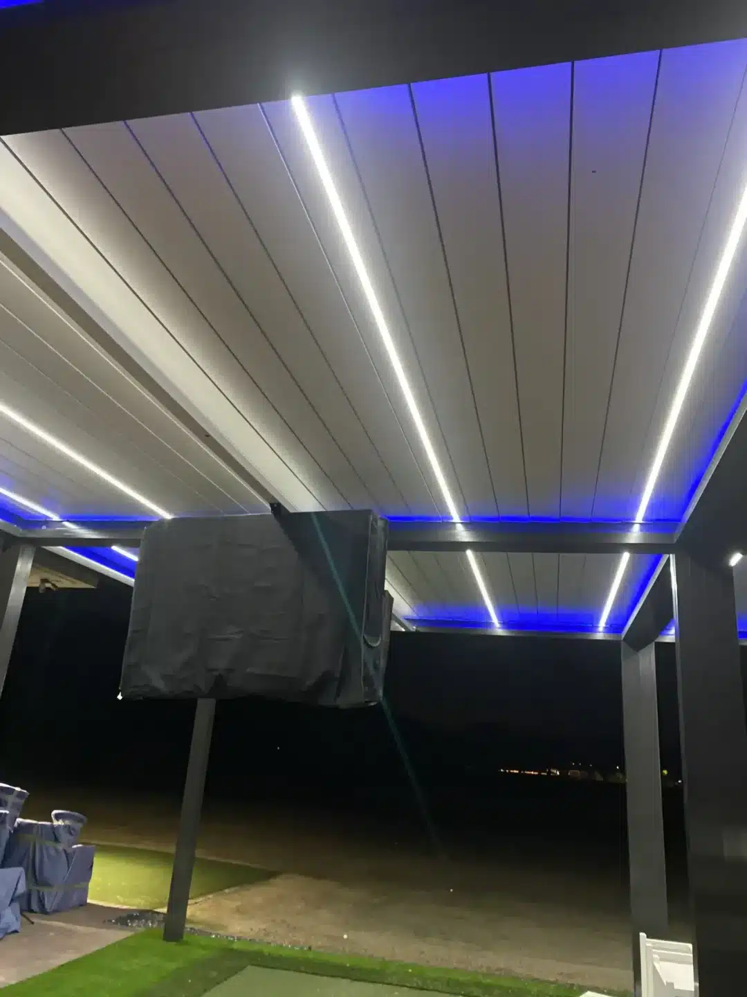 Outdoor space with a white paneled ceiling and blue LED strip lighting at night.