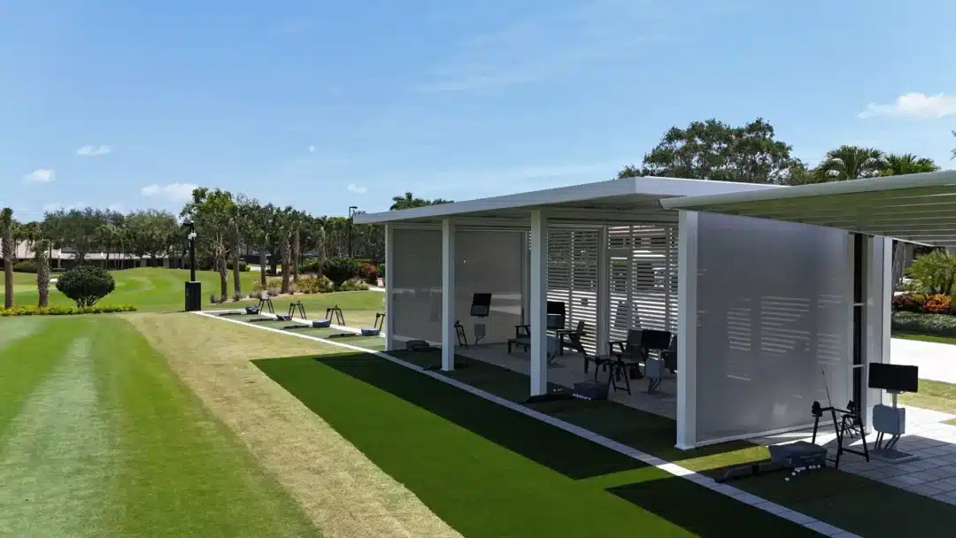 Outdoor golf practice bays with turf, hitting mats, and a white covered training pavilion on a sunny day