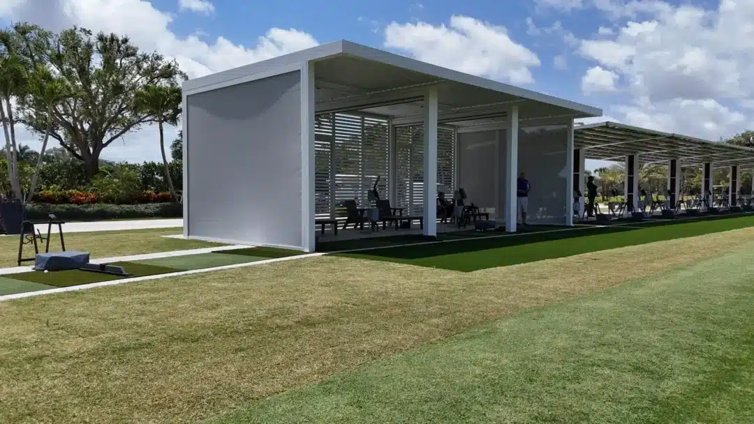 Modern open-air golf range with white-framed bays, slatted walls, and players practicing under a covered structure.