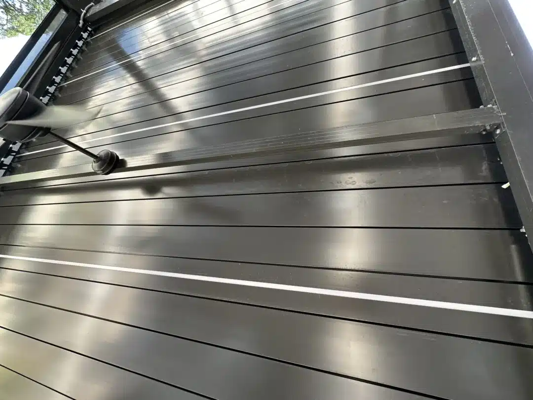 Close-up of a glossy metal rolling shutter with evenly spaced horizontal slats and a tension pulley on the left edge.